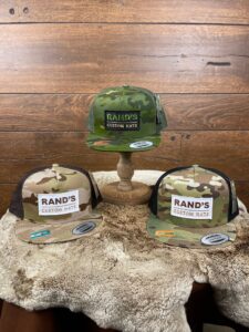 The Classic Yupoong Snapback hats with Rand’s Custom Hats patch on the front. From left to right: Multicam Arid camo and brown mesh; Green Tropic Camo; and Multicam Camo with black mesh
